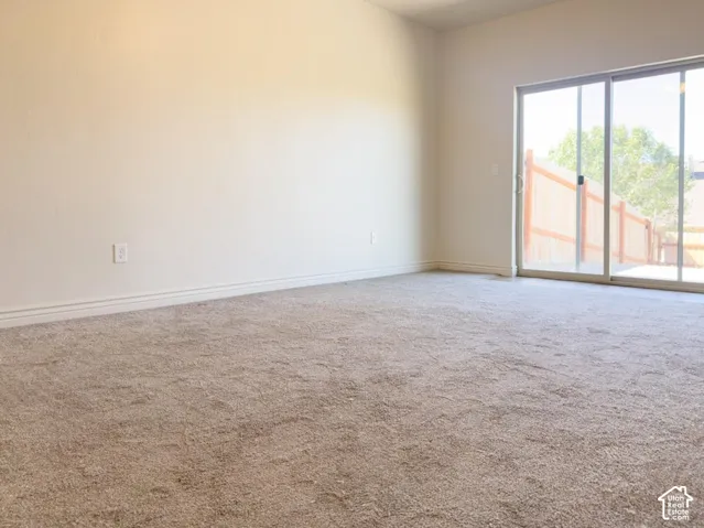 Neutral-toned wall-to-wall carpeting and sliding glass doors opening to an outdoor space with wood fencing