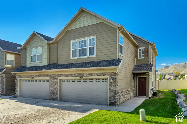 Multi-level exterior featuring horizontal lap siding, stone veneer accents, shake shingle gables, dual two-car garage bays, and a concrete driveway