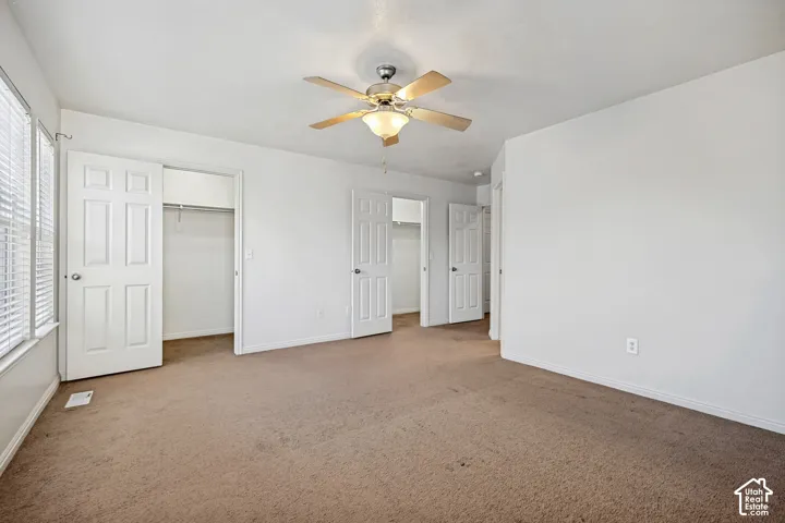 Room featuring neutral carpeting, white six-panel interior doors, multi-pane windows, and a central ceiling fan with integrated lighting
