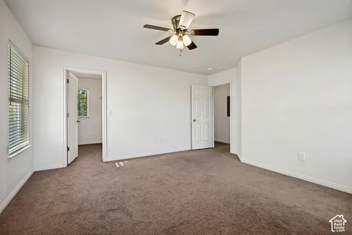 Neutral-toned carpeted flooring, multi-pane window with white trim, ceiling fan with integrated lighting, and two six-panel interior doors