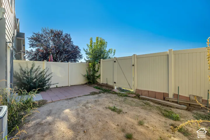 Fenced outdoor area featuring a concrete patio and mature shrubbery