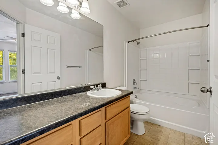 Bathroom featuring a wood-finish vanity with a stone-composite countertop, integrated sink, full-width vanity mirror, and a combination tub and shower with a molded surround
