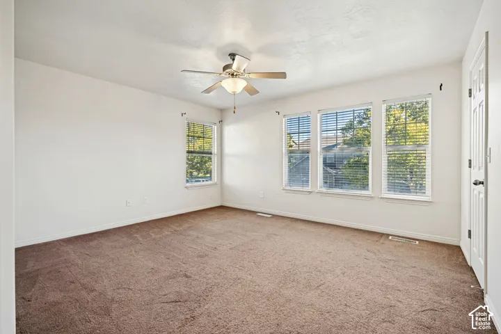 Interior space featuring neutral wall tones, wall-to-wall carpeting, multiple windows with horizontal blinds, and a central ceiling fan with integrated lighting