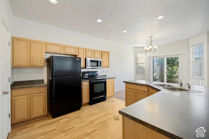 Kitchen featuring wood-finish cabinetry, an expansive peninsula with dual-basin sink, integrated black appliances, wood-finish flooring, and recessed ceiling lighting