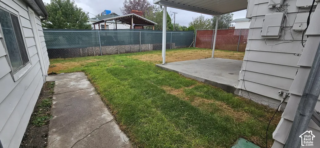 Backyard featuring a concrete patio, attached metal carport, and chain-link perimeter fencing