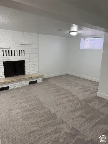 White painted brick fireplace featuring a stone hearth, neutral carpeting, and a flush-mount ceiling light