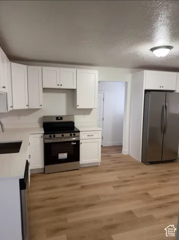 Kitchen featuring white shaker-style cabinetry, white solid-surface countertops, wood-finish flooring, and stainless steel appliances