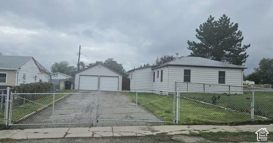 Single-level home featuring horizontal siding, a detached two-car garage, and a gated chain-link fence encompassing the lot