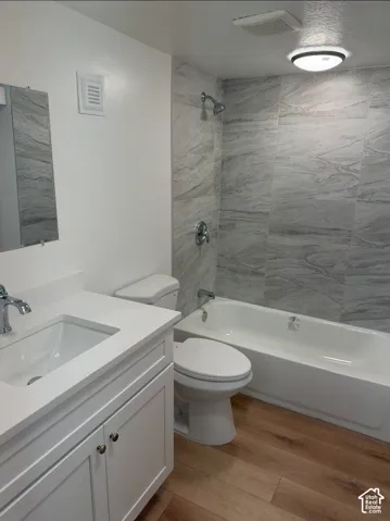 Bathroom featuring wood-finish flooring, a white vanity with a rectangular undermount sink, quartz countertop, and a shower-tub combination with large-format grey tile surround
