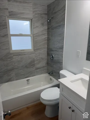 Full-height wall tiling with a natural stone-patterned finish, white shaker-style vanity with an integrated basin, wood-finish flooring, and a standard bathtub-shower combination with polished chrome fixtures