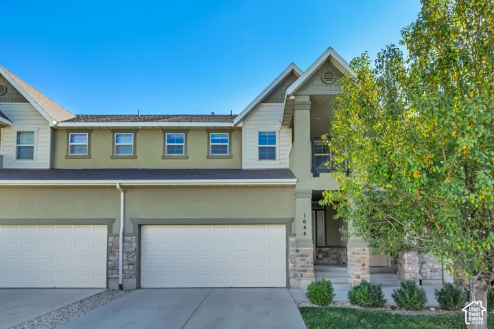 Multi-level exterior featuring stucco and stone veneer siding, dual-car garage, covered entryway, and shingle roofing