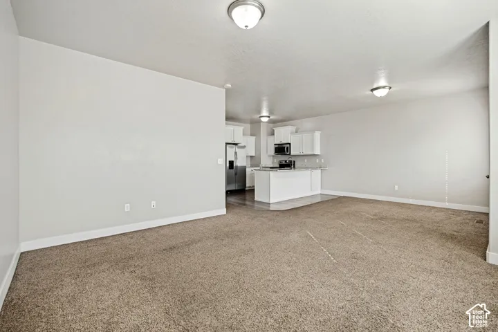 Neutral-toned carpeted flooring, white cabinetry, integrated stainless steel appliances, and flush-mount ceiling lighting