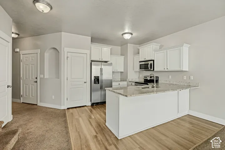 Kitchen featuring white cabinetry, stone countertops, stainless steel refrigerator, built-in microwave, and wood-finish flooring