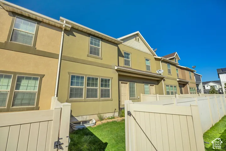 Multi-level exterior featuring stucco siding, gabled rooflines, vinyl fencing, and a grass-covered backyard