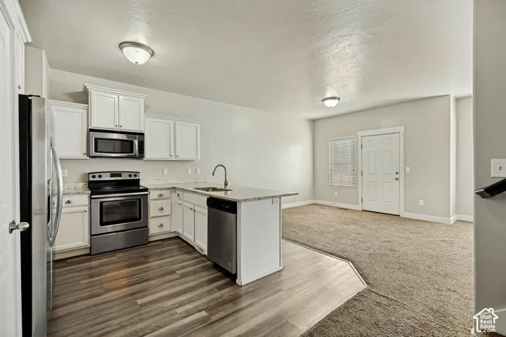 Kitchen featuring white cabinetry, stone-surface countertops, stainless steel appliances, and wood-finish flooring