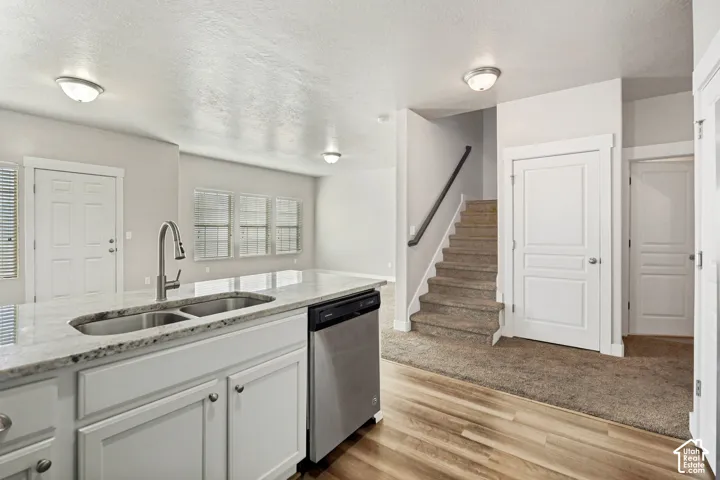 Kitchen featuring a stone-look countertop, undermount double-basin sink with gooseneck faucet, white cabinetry, stainless steel dishwasher, and wood-finish flooring