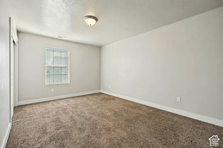 Neutral-toned interior space featuring wall-to-wall carpeting, a single-hung window with blinds, and a dome-style flush mount ceiling light