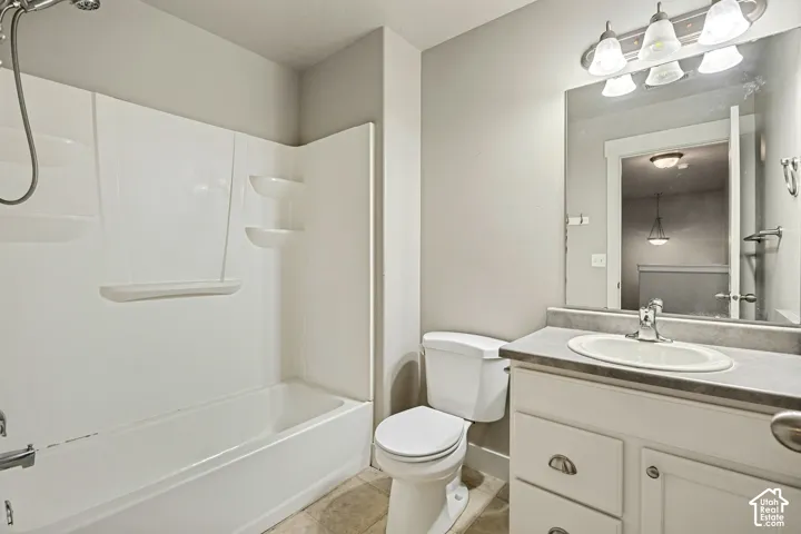 Full bathroom featuring a white composite tub-shower surround, vanity with an integrated oval sink, stone-finish countertop, large wall-mounted mirror, and multi-bulb vanity lighting
