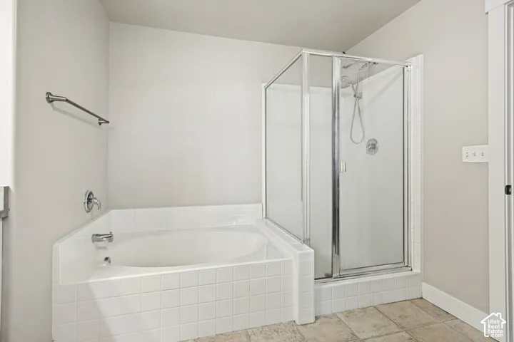 Bathroom featuring an oval soaking tub with a tiled surround, a glass-enclosed shower, polished chrome fixtures, and neutral tile flooring