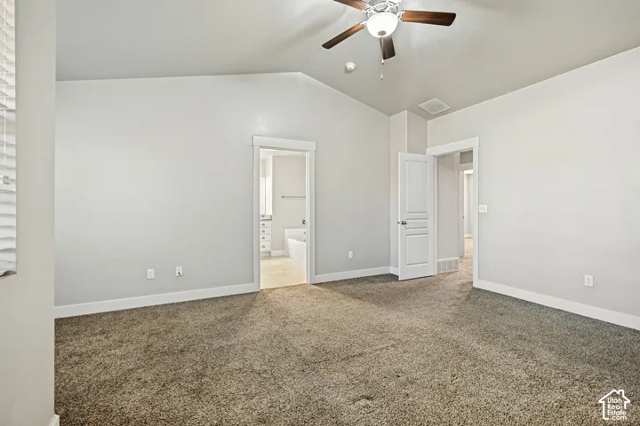 Vaulted ceilings, neutral carpeting, and a ceiling-mounted light fixture with fan