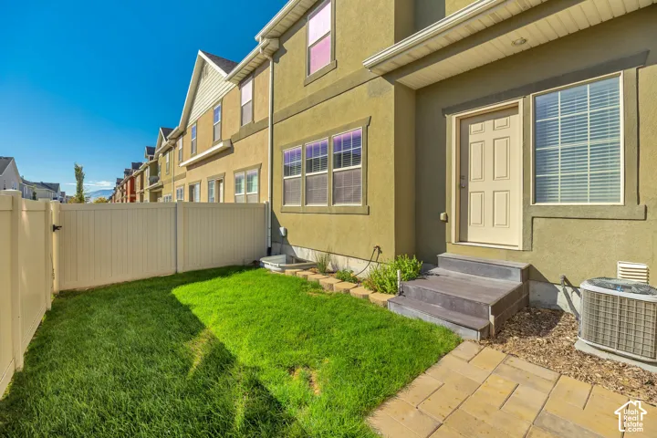 Stucco exterior featuring a vinyl privacy fence, landscaped lawn, stone-paver patio, and low-profile steps
