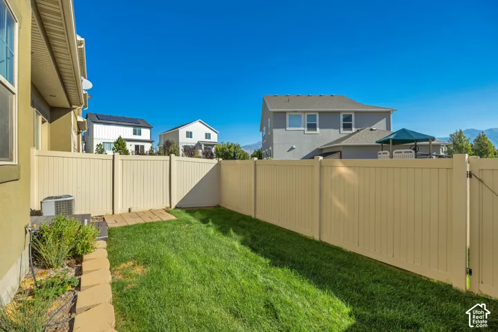 Backyard featuring a vinyl privacy fence, manicured lawn, stone border edging, and paved patio area