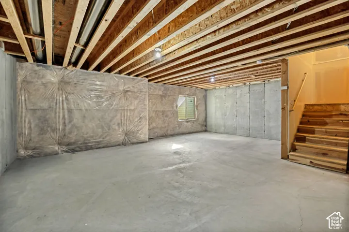 Unfinished interior space featuring exposed wood joist ceilings, poured concrete foundation walls with vapor barrier insulation, concrete flooring, and wooden staircase