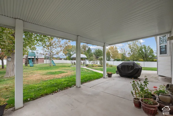 Covered concrete patio with overhead lighting, featuring a spacious lawn enclosed by perimeter fencing