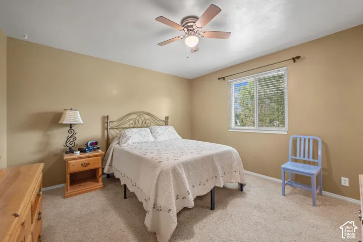 Room featuring neutral wall tones, wall-to-wall carpeting, a multi-blade ceiling fan with integrated lighting, and a single-pane horizontal window with an adjustable metal curtain rod