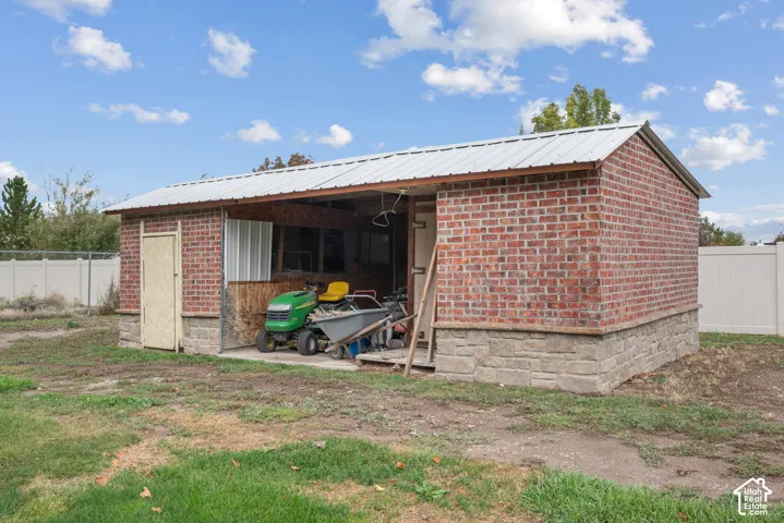Outbuilding featuring red brick masonry, a metal roof, stone-textured foundation, and a concrete slab base