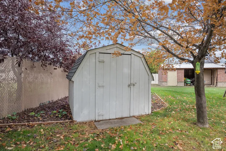 White gambrel-style storage shed featuring dual entry doors, shingled roofing, and a metal latch mechanism