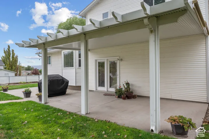 Covered concrete patio featuring a structural pergola, vinyl siding, and dual-pane glass entry doors