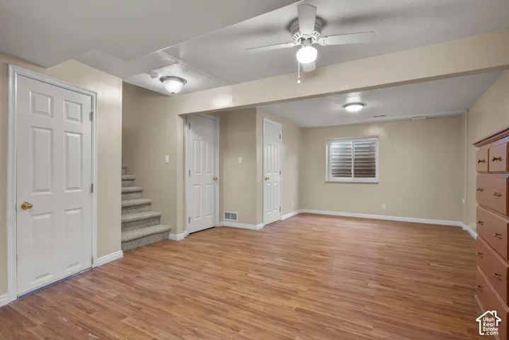 Interior space featuring wood-finish flooring, white panel doors, neutral wall tones, a ceiling fan with integrated lighting, and a single window with shutter-style blinds