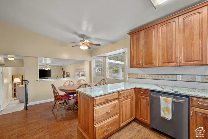 Kitchen featuring wood cabinetry, stone countertops, a tile backsplash, stainless steel dishwasher, and wood-finish flooring