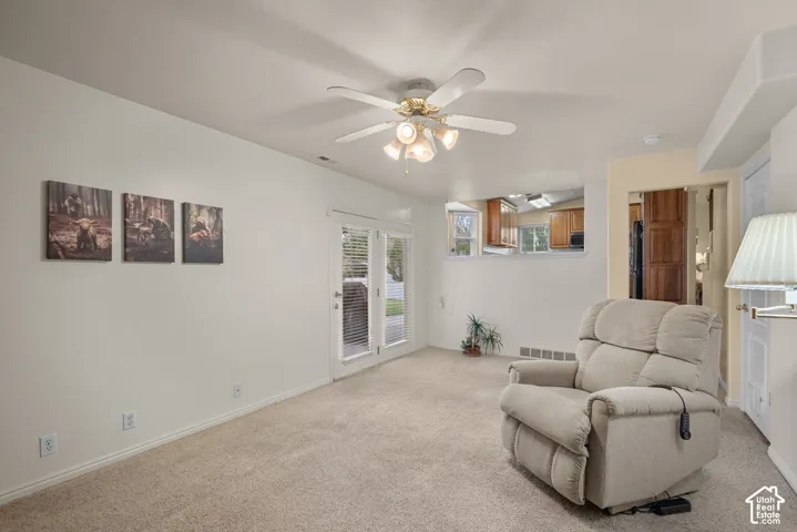 Neutral-toned interior featuring wall-to-wall carpeting, a ceiling-mounted light fixture with four-blade fan, double-panel glass door, and a pass-through opening