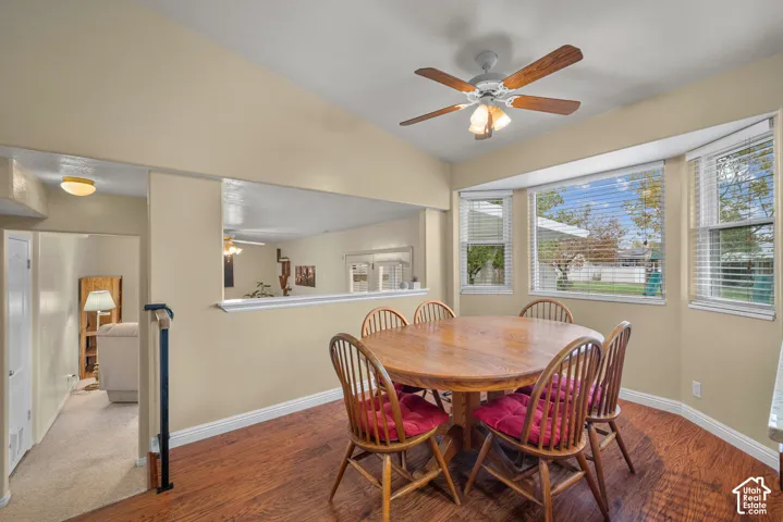Vaulted ceilings, wood-finish flooring, bay windows, and a ceiling fan with integrated light fixture