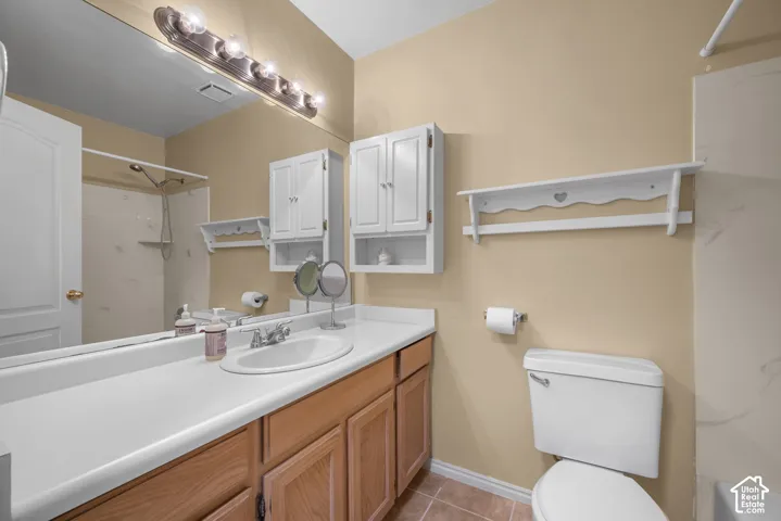 Bathroom featuring a wood-finish vanity with a white countertop and oval undermount sink, large wall-to-wall mirror, multi-bulb overhead lighting, white wall-mounted cabinetry, and tile flooring