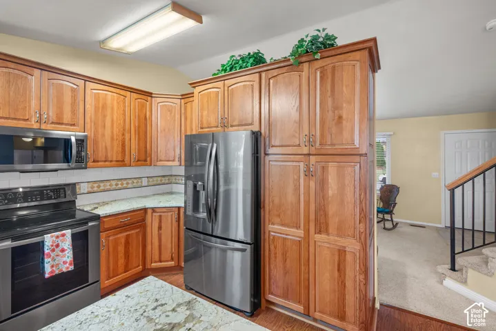 Kitchen featuring wood cabinetry, stone-surface countertops, stainless steel appliances, and an integrated full-height pantry cabinet