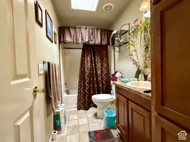 Bathroom featuring a skylight, wood-finish vanity cabinetry, integrated countertop with a drop-in sink, and a combination tub and shower enclosure