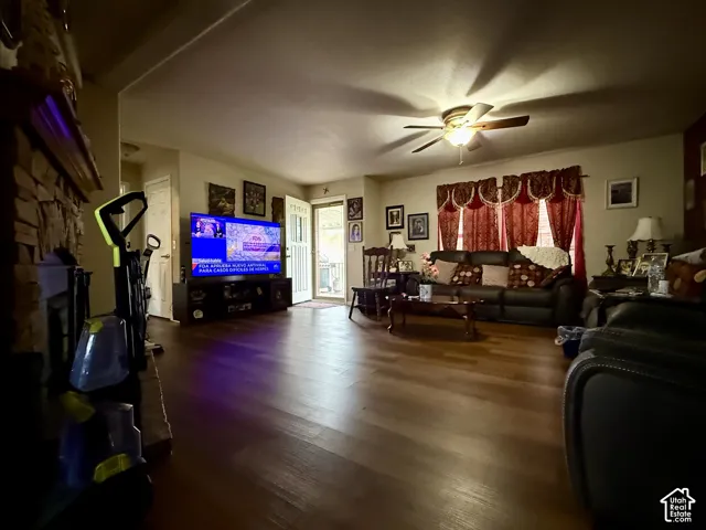 Living area featuring wood-finish flooring, stone-surround fireplace with a wooden mantel, and a ceiling fan