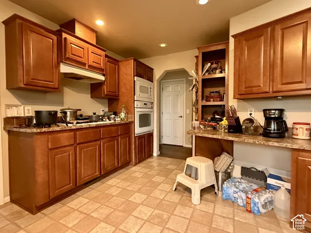 Kitchen featuring warm-tone wood cabinetry, stone-finish laminate countertops, built-in dual oven, recessed ceiling lighting, and tile flooring