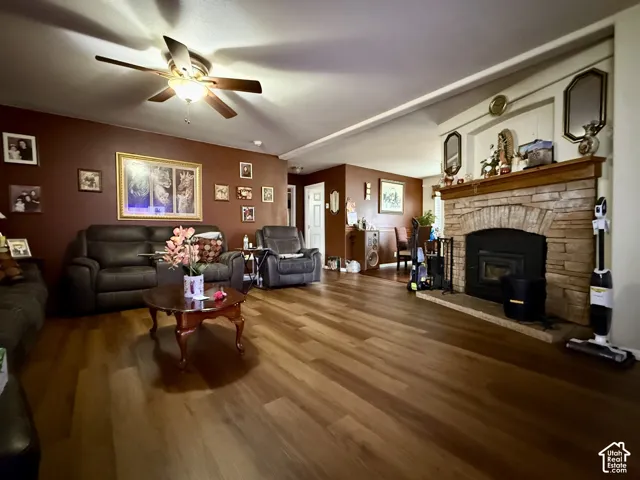 Wood-finish flooring, fireplace with stone surround and arched brick detail, built-in recessed mantle shelf, and ceiling fan with integrated lighting