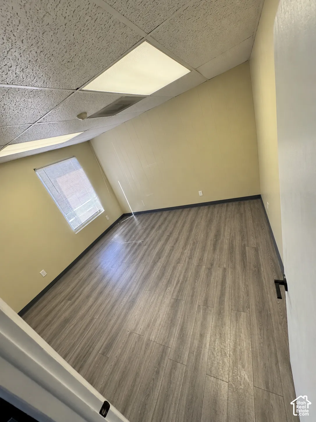 Interior room featuring wood-finish flooring, neutral wall tones, a recessed window, and drop ceiling panels with integrated lighting