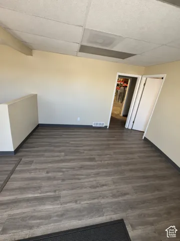Interior space featuring wood-finish flooring, neutral wall tones, a drop ceiling, and a half-height partition wall