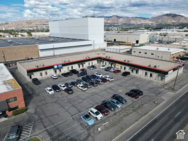 Single-story commercial building featuring an L-shaped structure, extensive asphalt parking area, and a mountain backdrop
