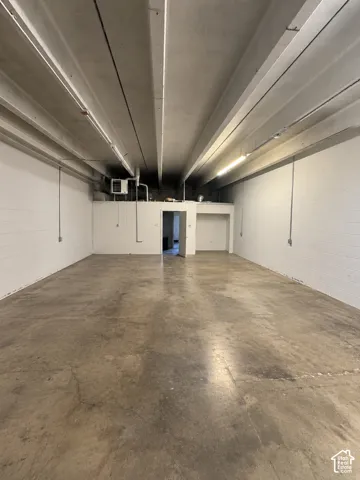 Expansive interior space featuring exposed structural ceiling beams, concrete flooring, painted masonry walls, and linear lighting fixtures