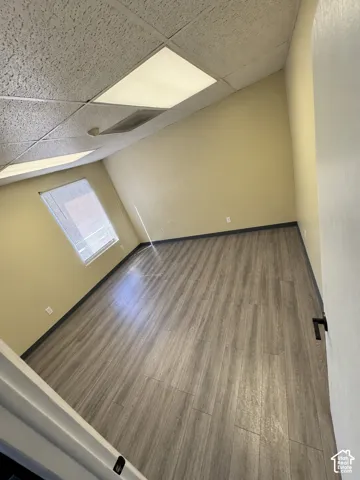 Interior room featuring wood-finish flooring, neutral wall tones, a recessed window, and drop ceiling panels with integrated lighting