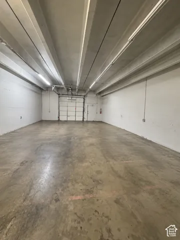 Spacious interior featuring exposed concrete walls, high ceilings with exposed structural beams, industrial concrete flooring, and a large metal roll-up door
