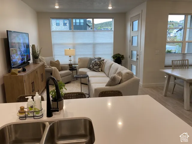 Integrated living area with wood-finish flooring, large windows, and a built-in kitchen sink with a matte black faucet
