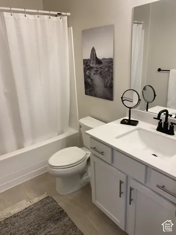 Bathroom featuring a built-in tub with shower, white vanity with an integrated sink, matte black faucet, and wood-finish flooring